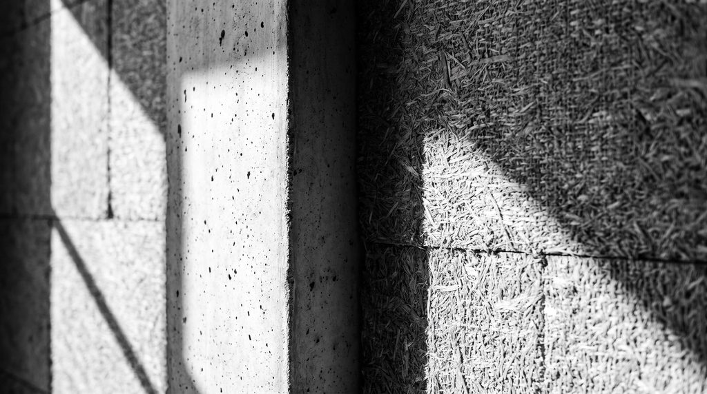 "Dettaglio architettonico in scala di grigi: texture del legno, cemento a vista e isolamento naturale in canapa"